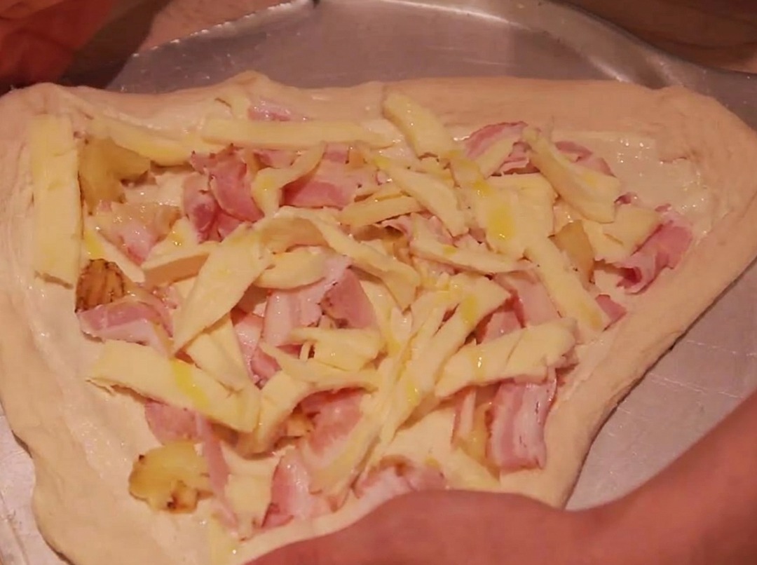 The edges of the pizza dough being folded inward to enclose the toppings.