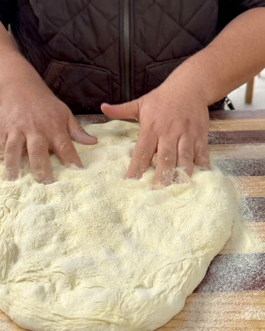 Flattened pizza dough resting on a parchment-lined baking sheet.