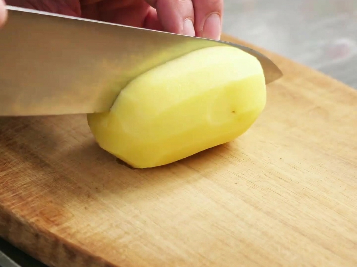 Raw potato chunks being prepared on a wooden cutting board.