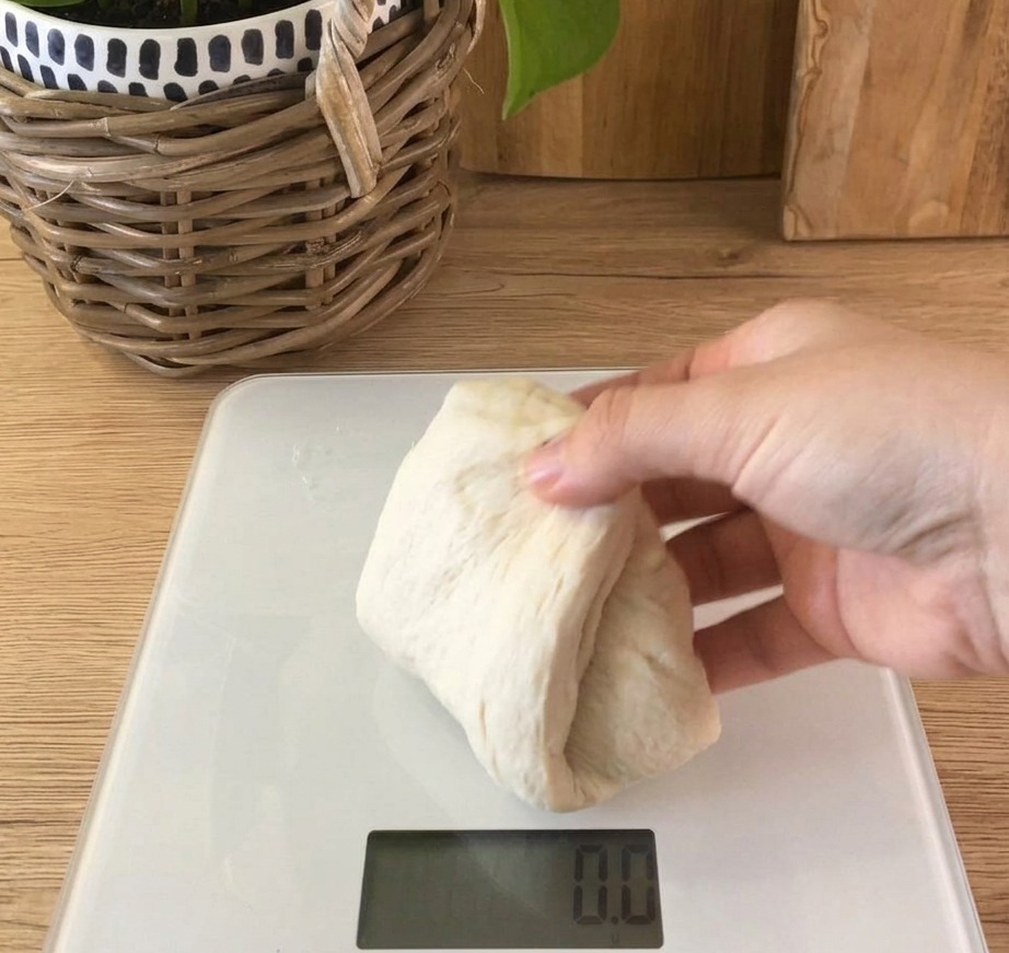A portion of soft, white bread dough resting on a digital kitchen scale displaying a weight.