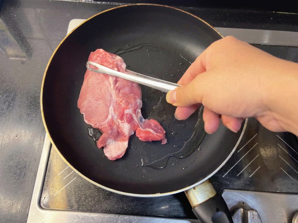 Two pieces of raw pork plum blossom meat searing in a hot frying pan.