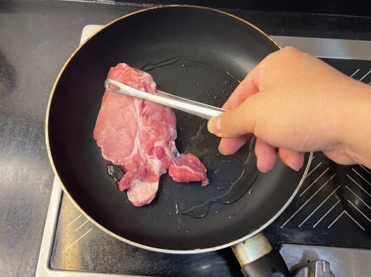 Tender, browned pork pieces being lifted from the pan with metal tongs.