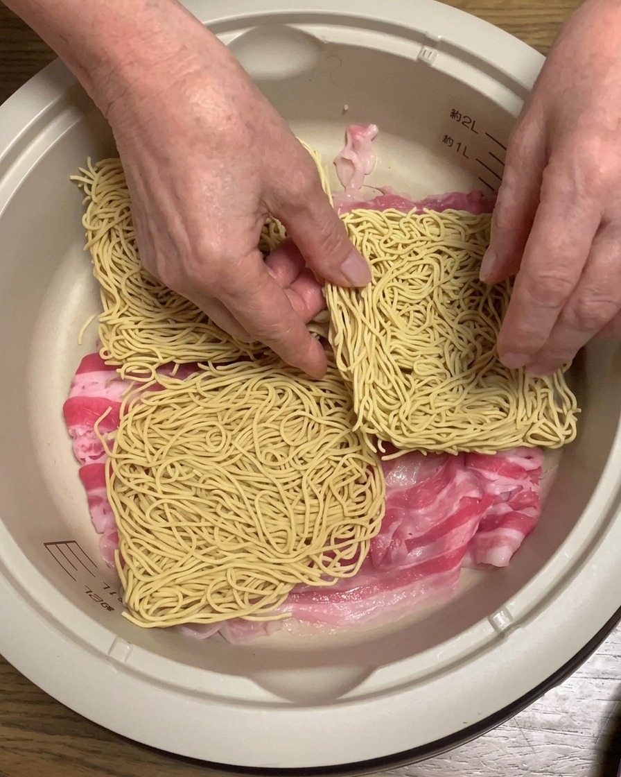 Dry ramen noodle blocks being layered onto the pork belly inside the pot.