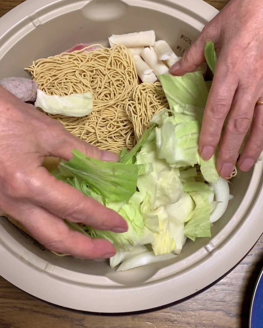 Fresh cabbage pieces and bright red crab sticks being placed into the pot.
