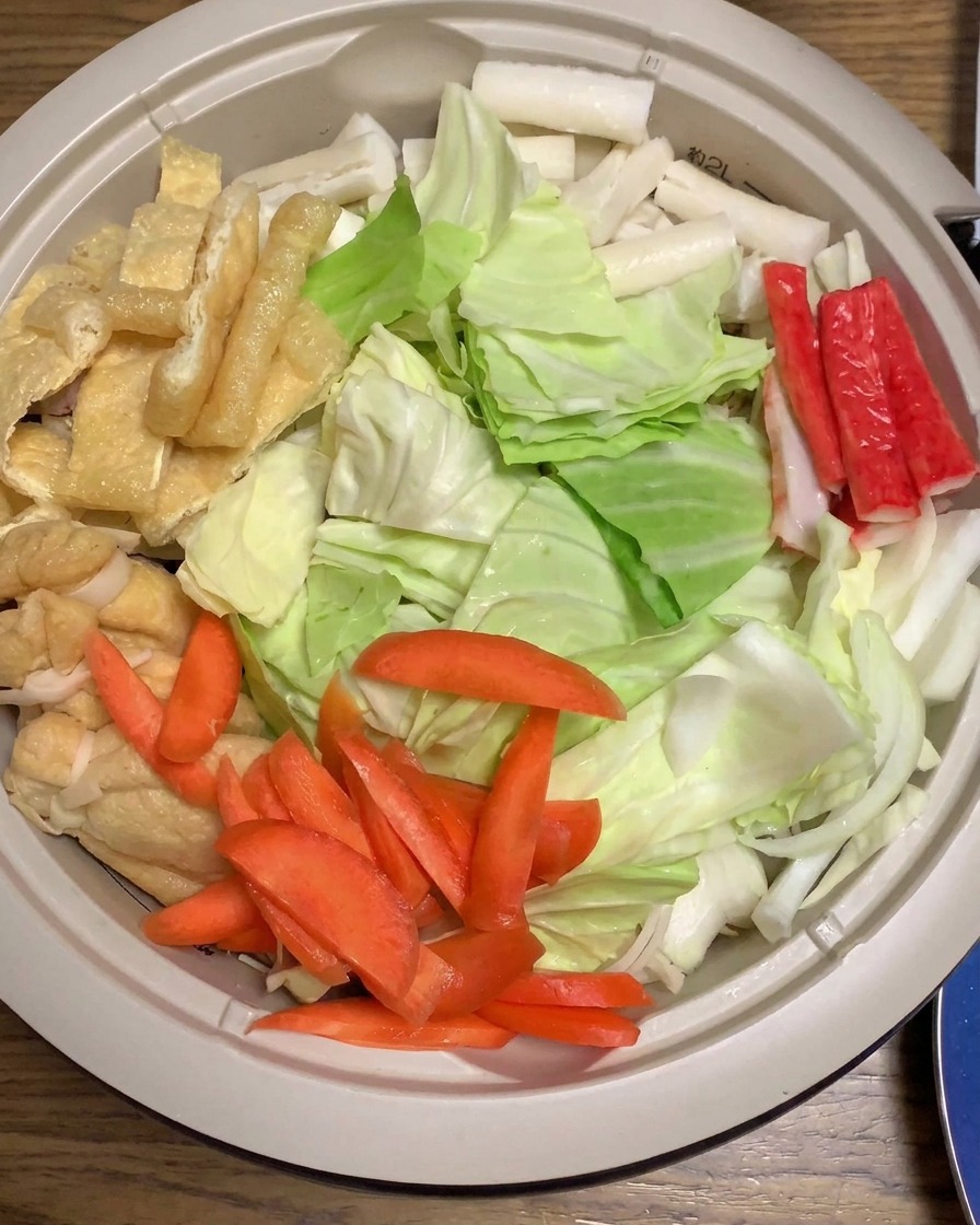 Miso sauce being poured over layered cabbage, carrots, crab sticks, and other ingredients in a large cooking pot.