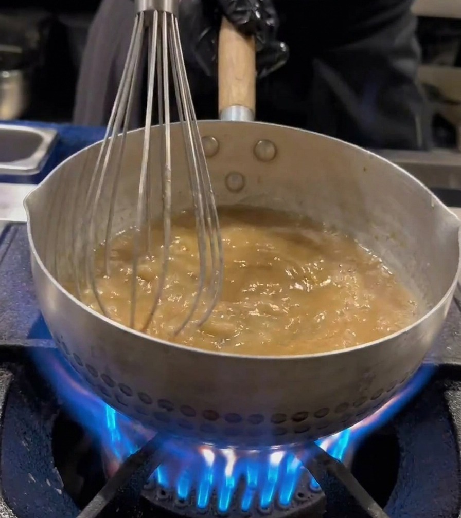 Ramen noodles being agitated with a wire whisk inside a boiling water pot.