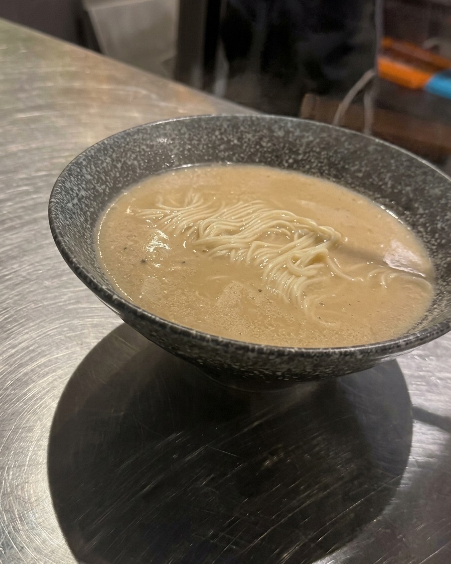 A spoonful of seasoned minced meat being lowered into the center of a bowl of ramen noodles in broth.