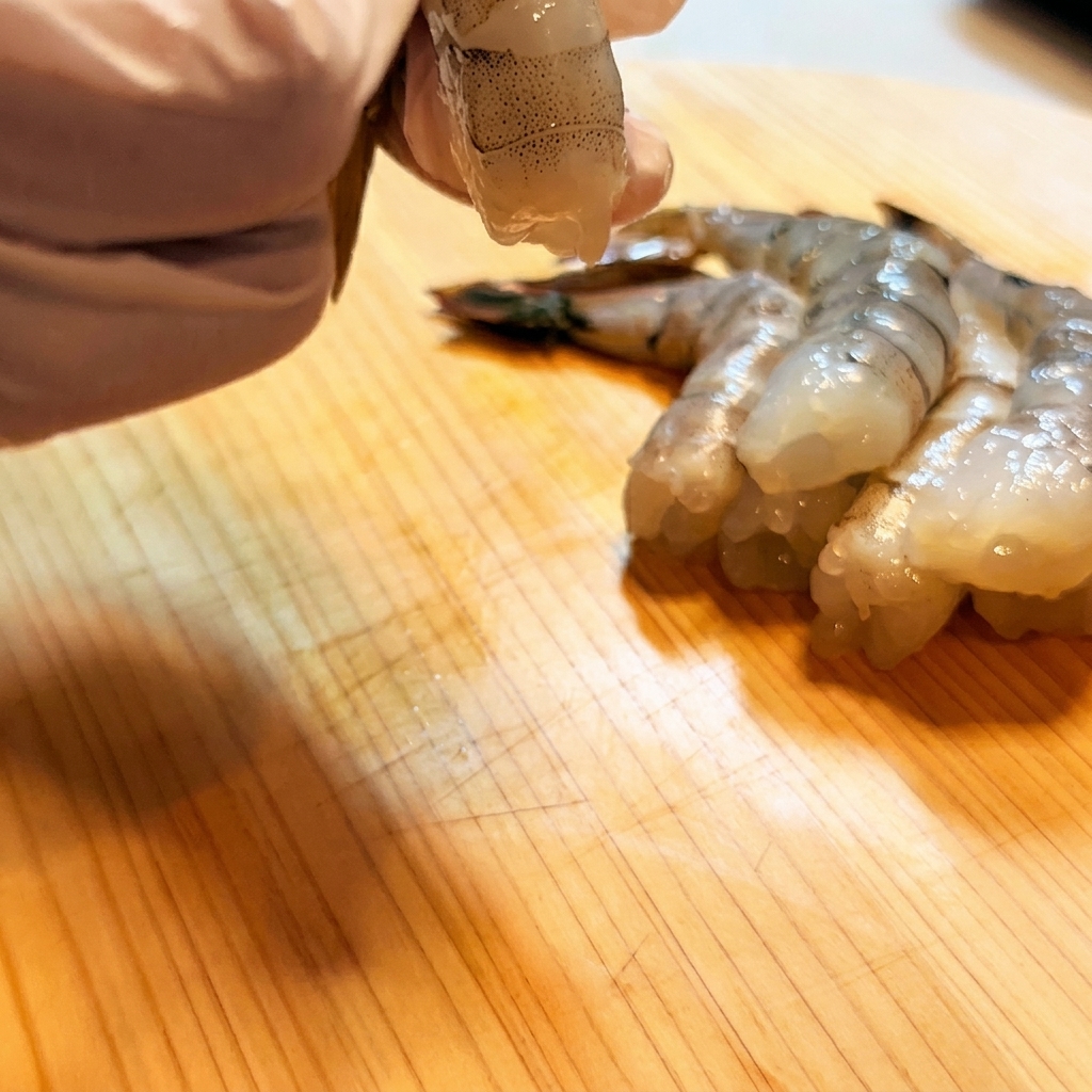 Shrimp being scored and straightened with a knife.