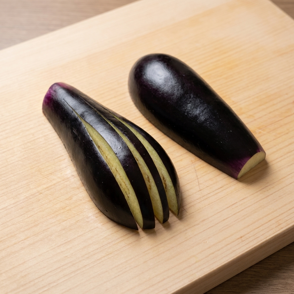 Eggplant being scored into a fan shape on a cutting board.