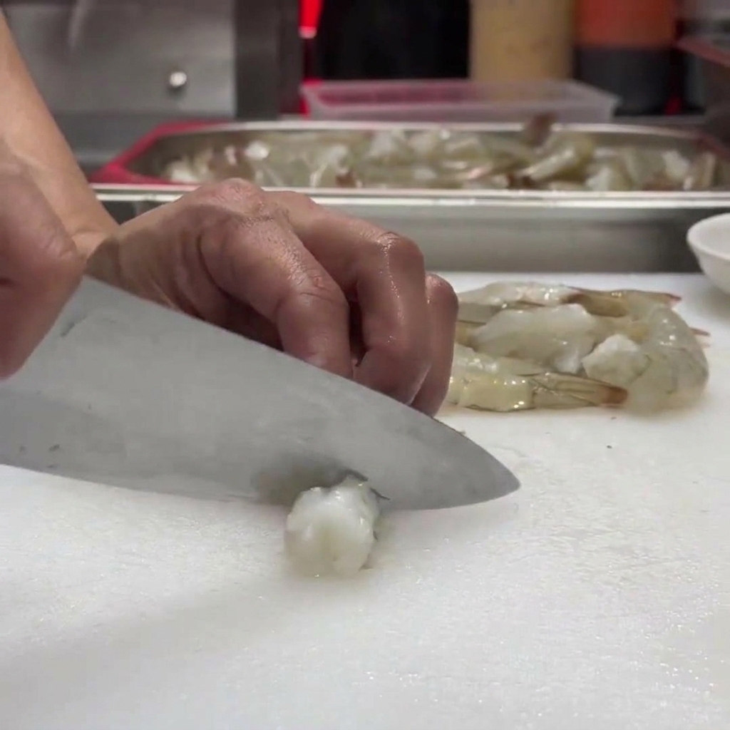 Knife making small, precise cuts along the underside of the raw shrimp.