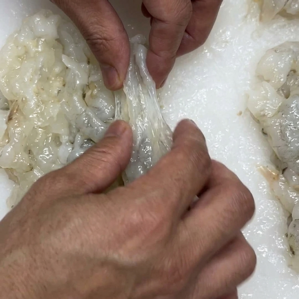 Hands stretching a prepared shrimp to elongate it before battering.