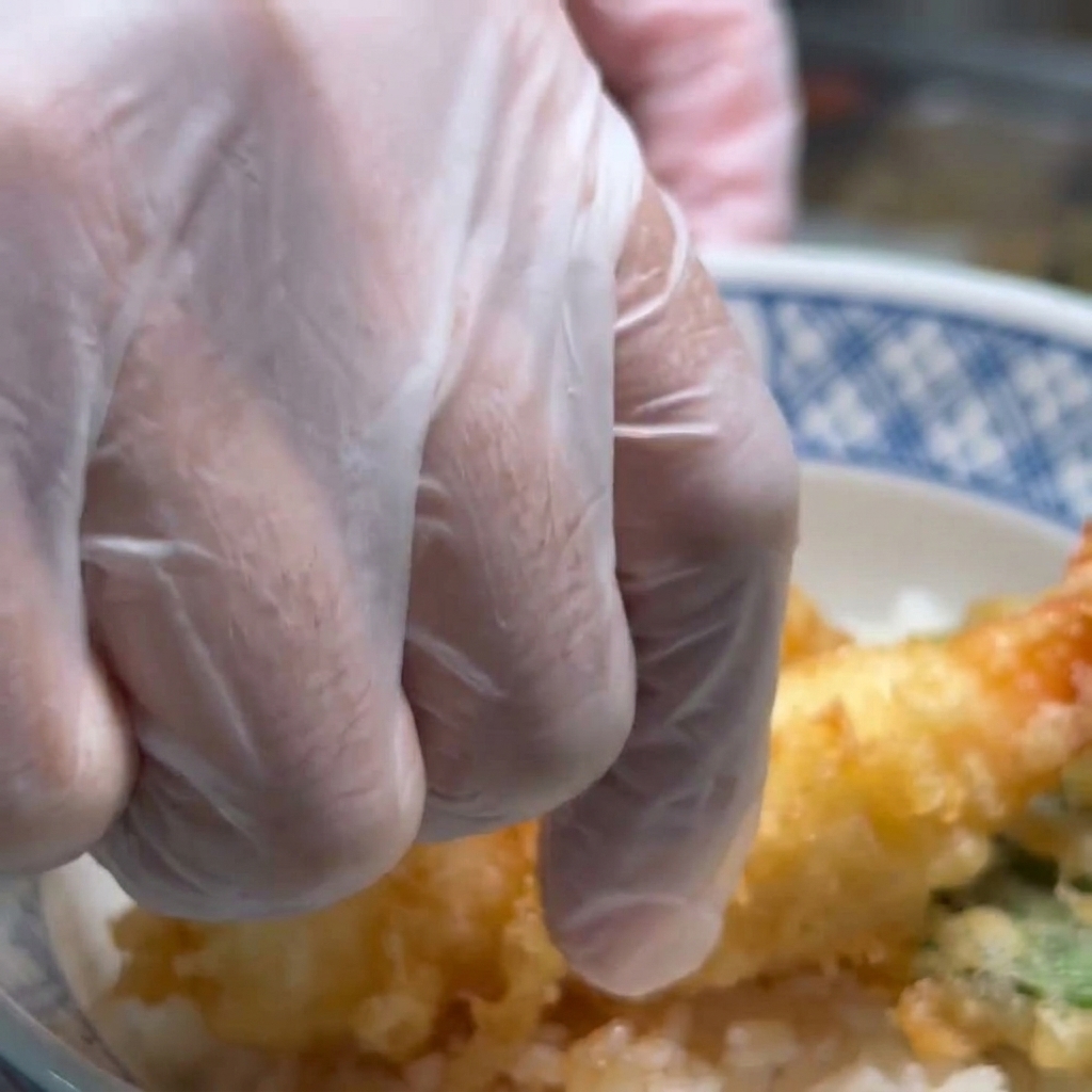 Fried shrimp being placed on a bed of white rice in a bowl, ready for garnishing.