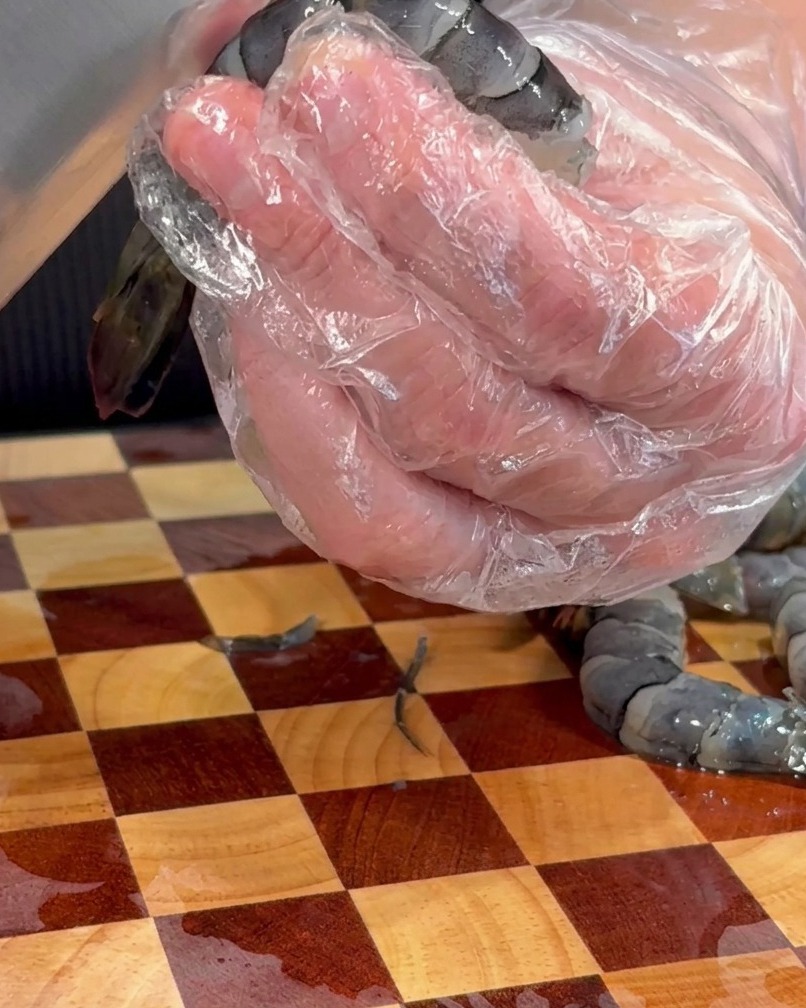 Close-up of a knife tip removing the dark vein from the back of a raw shrimp.