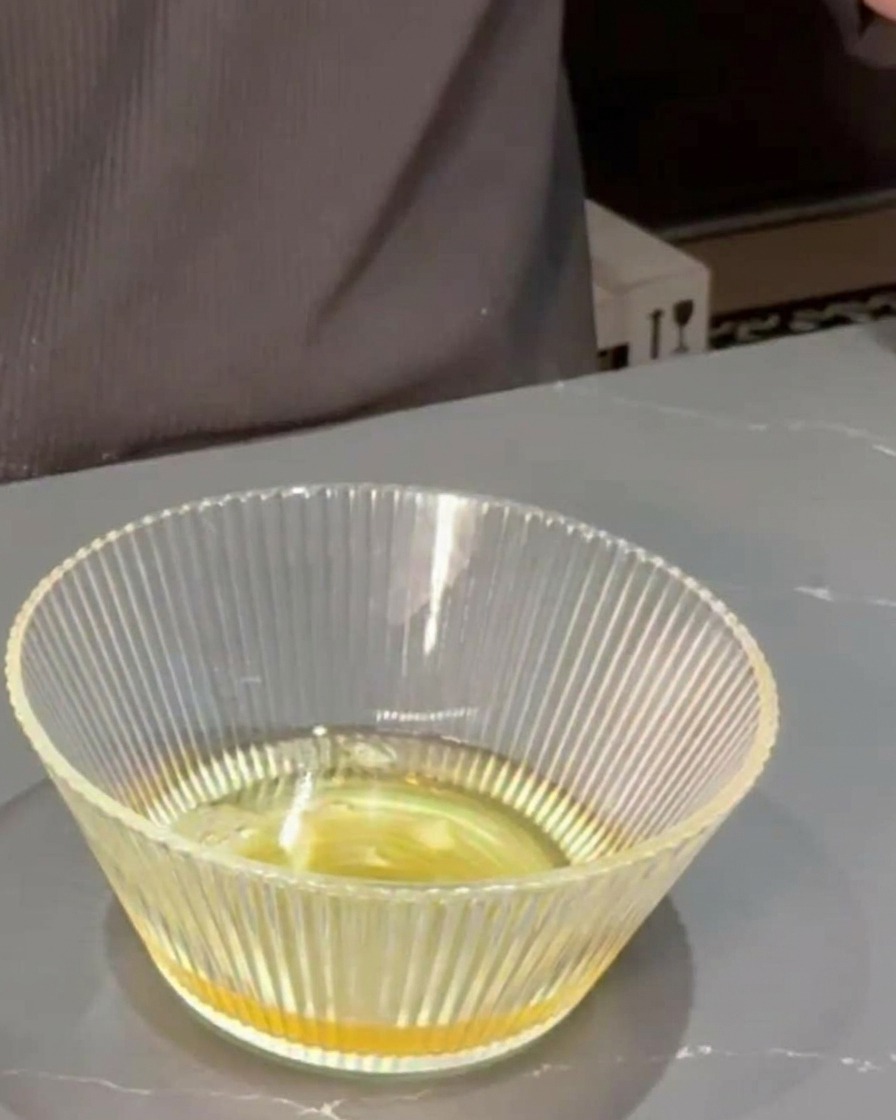 Mirin and soy sauce being poured into a clear glass bowl containing dashi stock.
