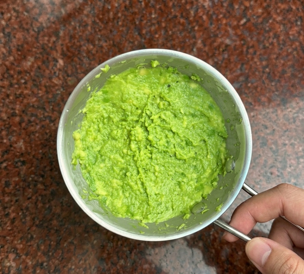 A metal fork mashing bright green avocado into a thick paste in a small bowl.