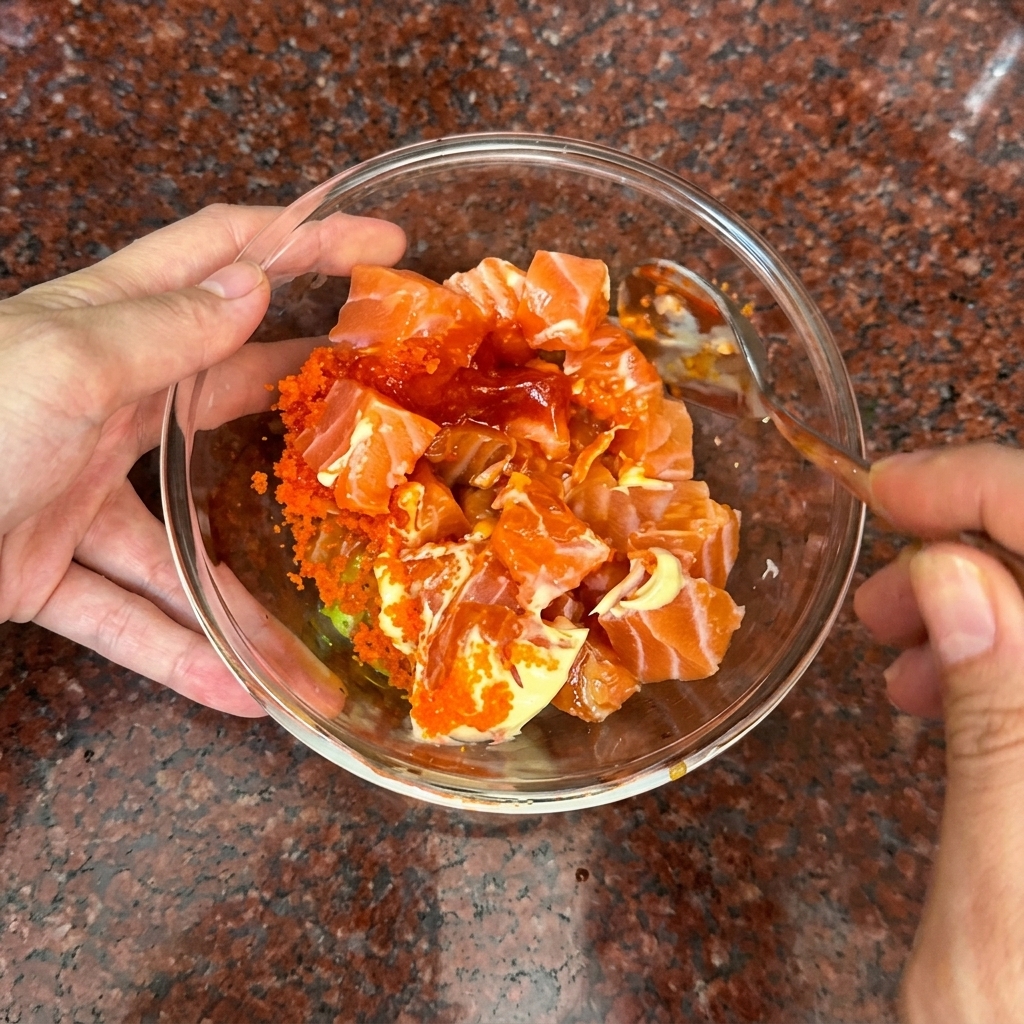 A hand stirring salmon cubes and creamy orange sauce together with a spoon.