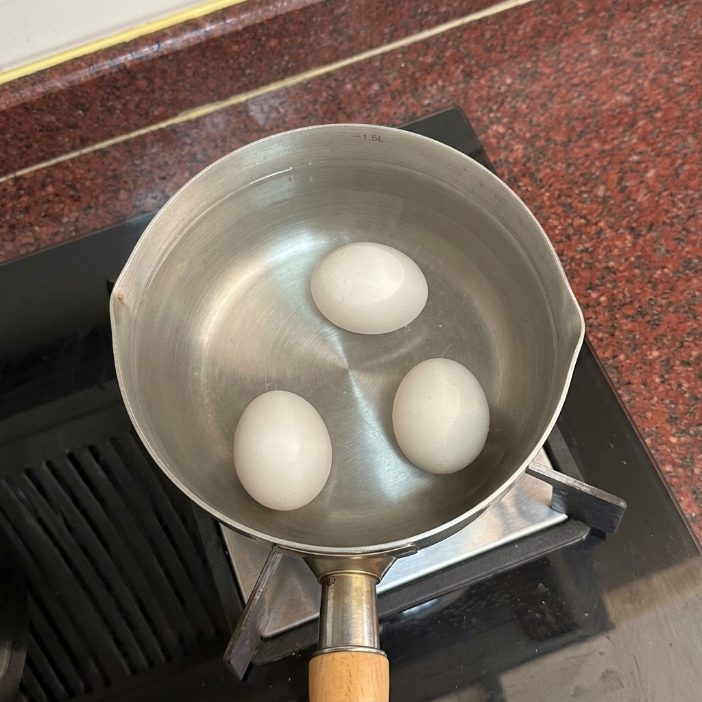 Three white eggs resting at the bottom of a pot filled with clear hot water.