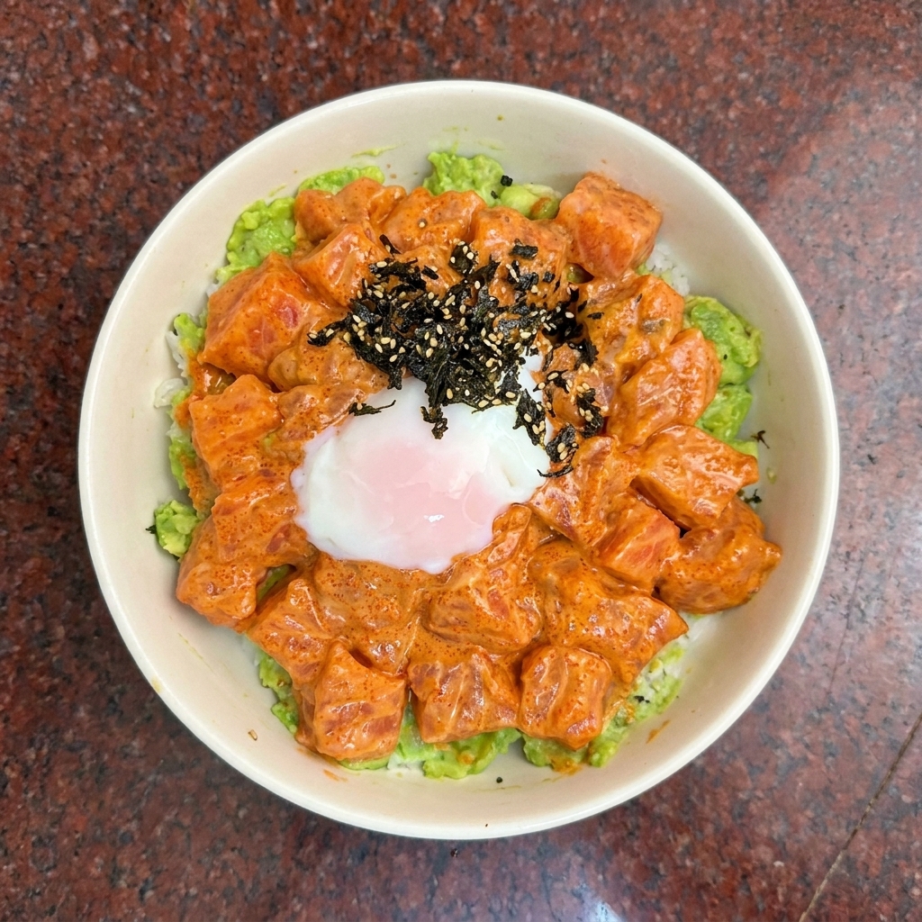A top-down view of a salmon poke bowl topped with a soft-boiled egg and dark seaweed seasoning.