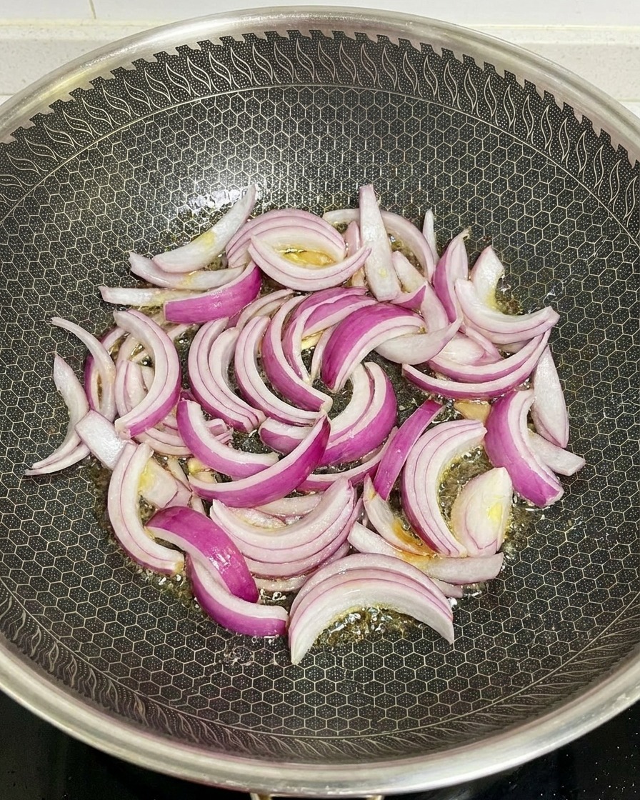 Red onion slices being stir-fried in a hot hexagonal-patterned wok with shimmering oil.