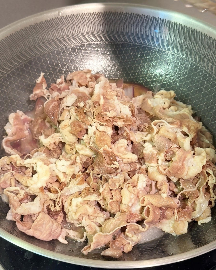 Tender blanched beef strips being mixed with red onions and dark sauce in a stainless steel wok.