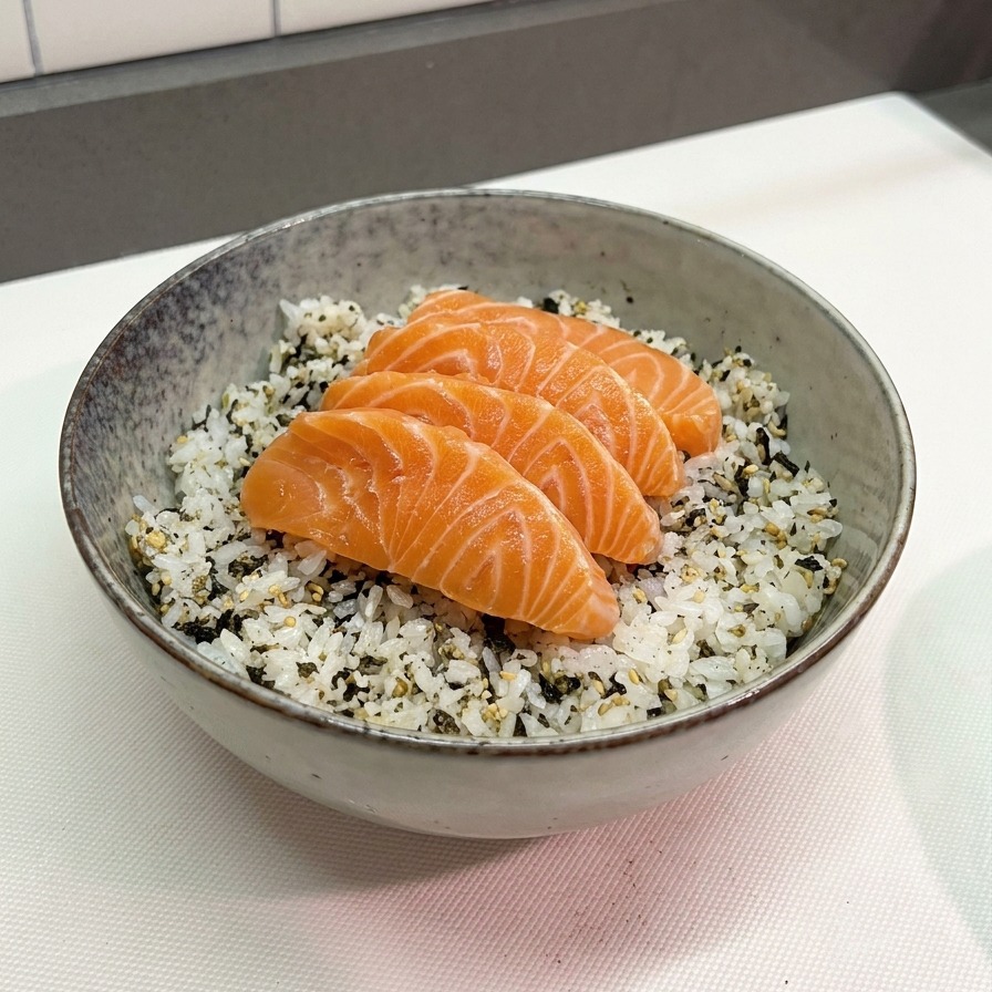 Four thick, vibrant orange salmon slices laid neatly over a bed of white rice speckled with black seaweed flakes in a grey ceramic bowl.