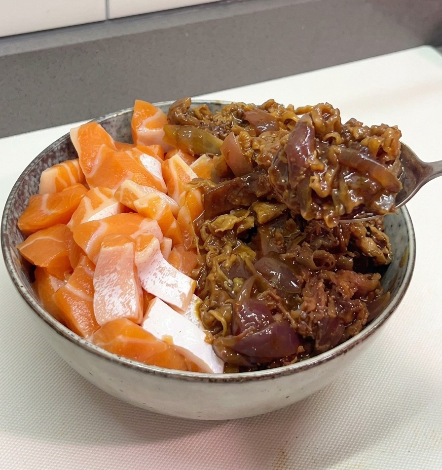 A metal spoon depositing a heap of saucy, stir-fried beef and purple onions into a bowl already containing fresh salmon pieces.