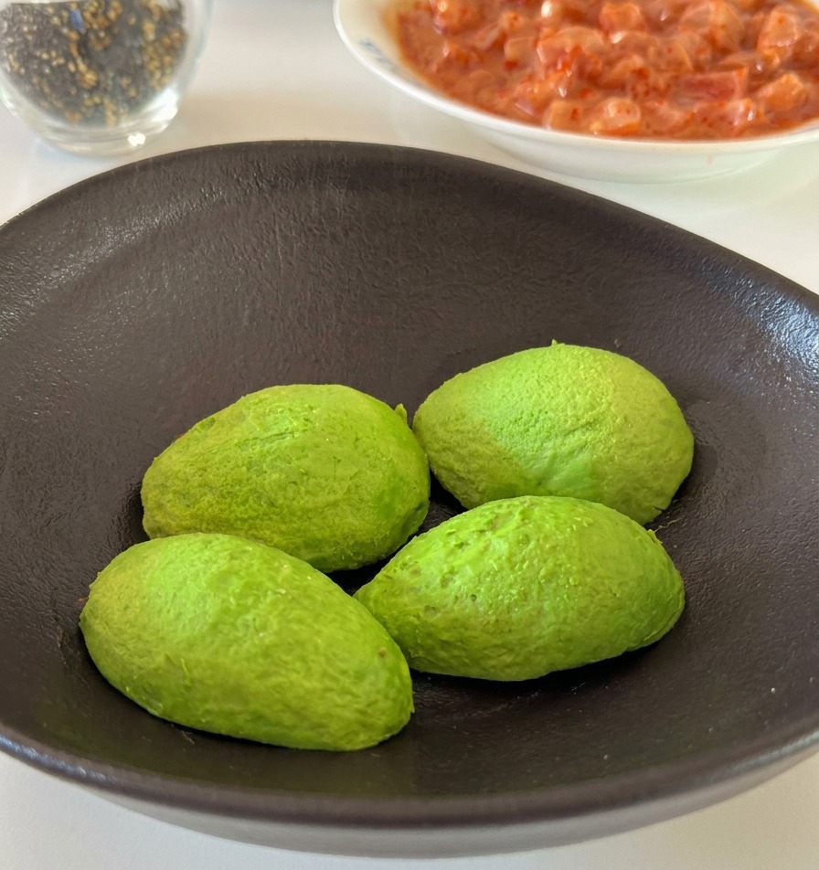 A hand squeezing a fresh lemon wedge over green avocado halves in a ceramic bowl.