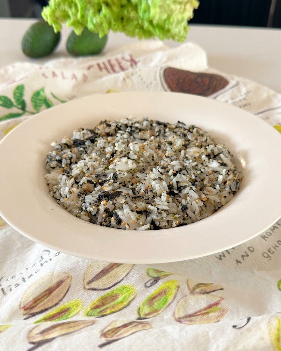 A white bowl filled with rice evenly covered with black and white sesame seeds and shredded green seaweed flakes.