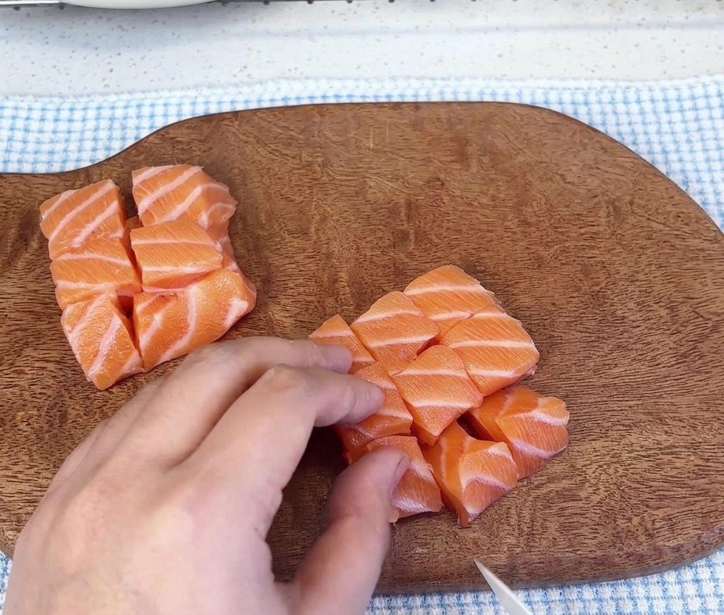 Several mounds of diced raw salmon cubes resting on a wooden cutting board after being sliced.