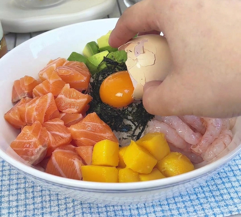 An orange egg yolk being poured from half an eggshell onto the seaweed garnish in the middle of the bowl.