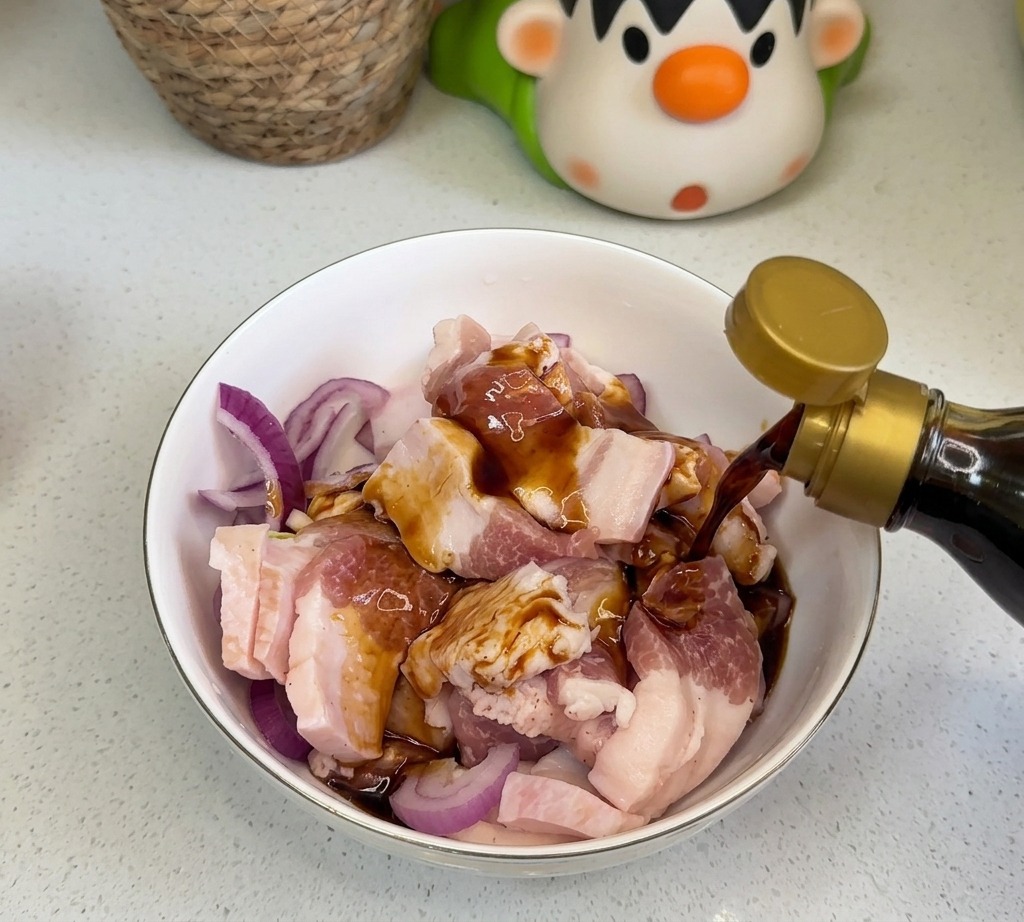 Dark liquid seasonings like soy sauce and oyster sauce being poured over raw pork belly and red onions in a bowl.