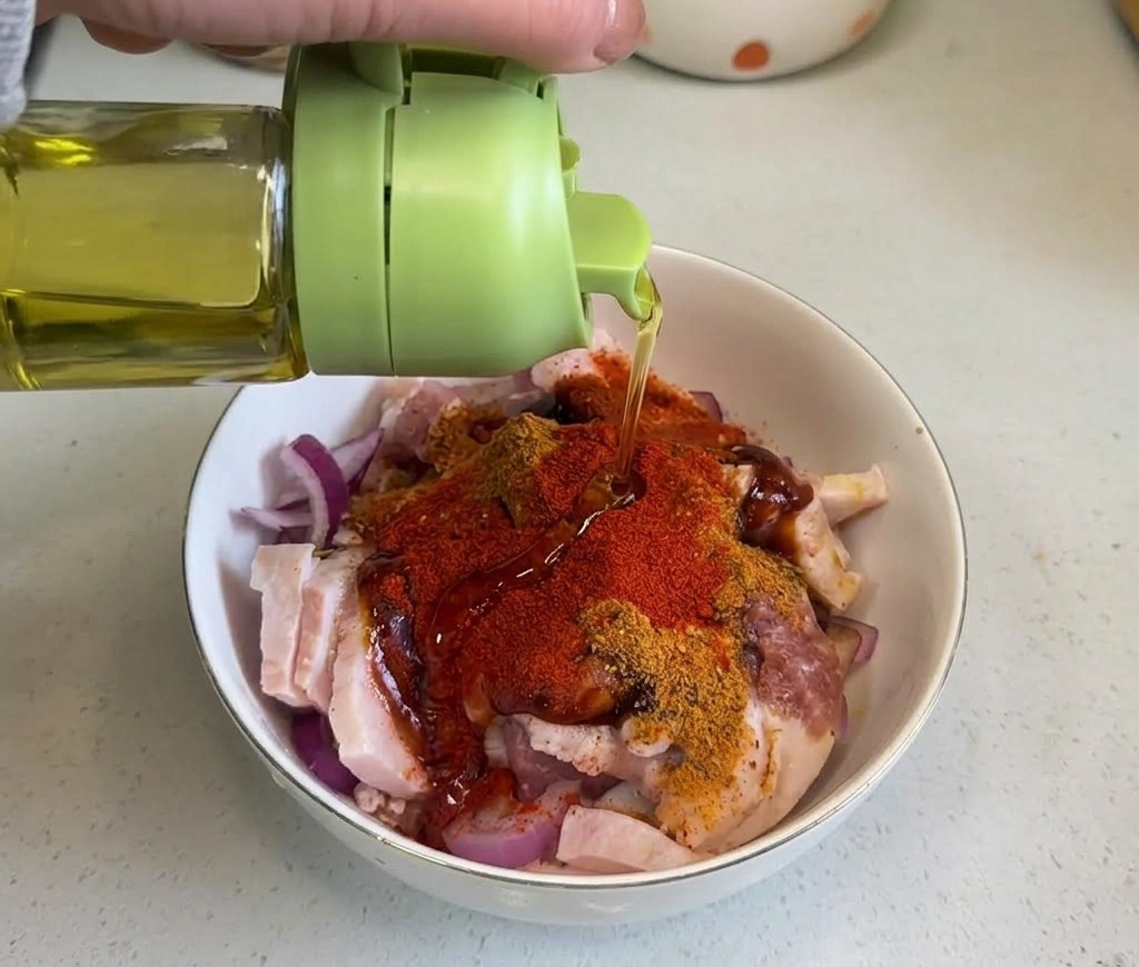 Clear cooking oil being drizzled from a green bottle onto the spiced pork belly mixture.