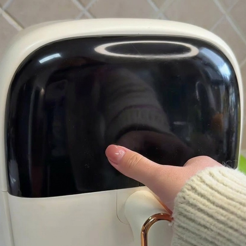 A close-up of a hand touching the sleek black digital control panel of a white air fryer.