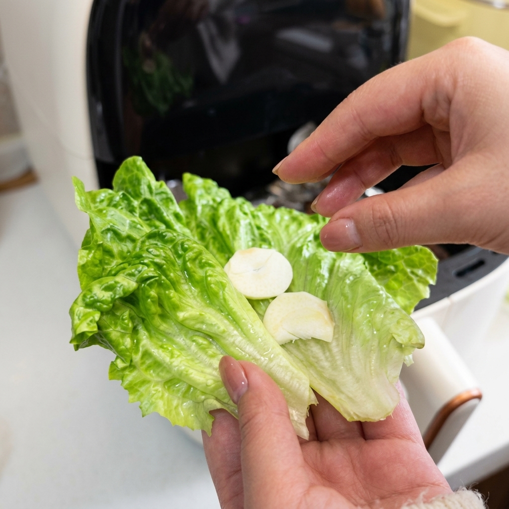 A close-up of a hand holding a green lettuce leaf topped with two slices of fresh white garlic.