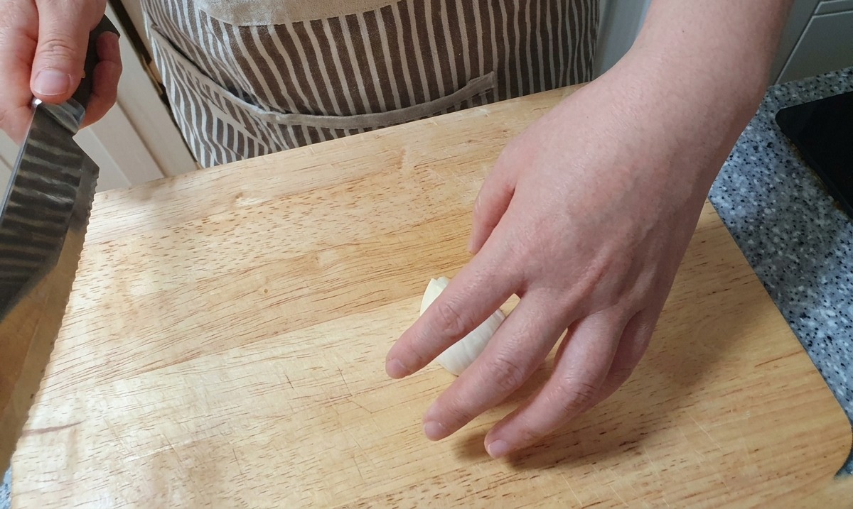 Using a knife to create thin, vertical slices of a white onion on a wooden surface.