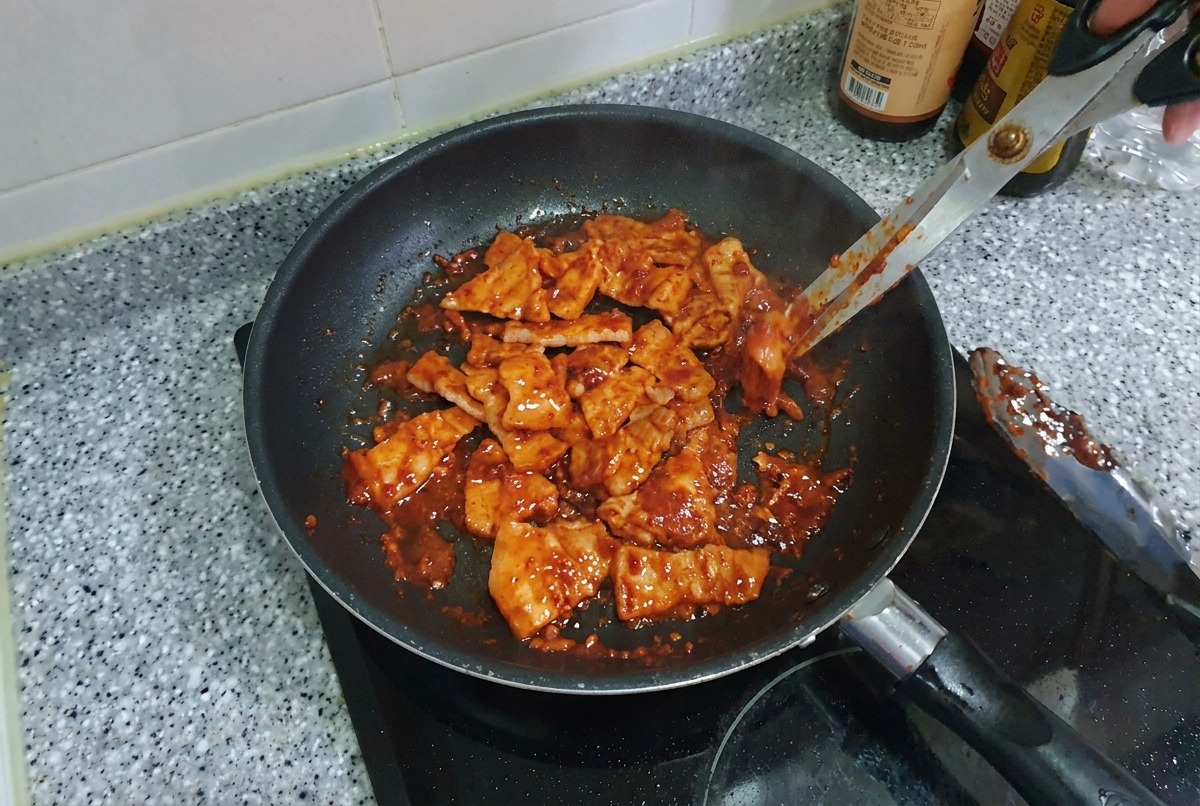 Bite-sized pieces of spicy pork belly being tossed in a pan, looking glossy and caramelized.