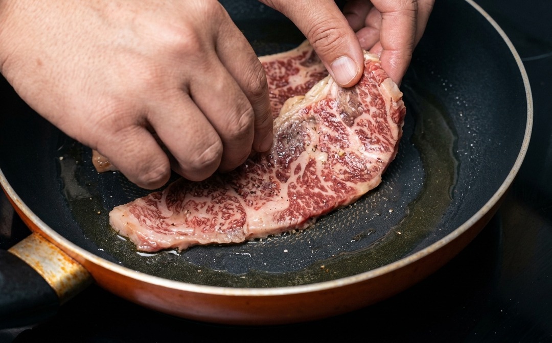 A hand placing a well-marbled, marinated beef short rib into a hot frying pan.