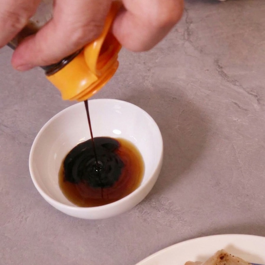Dark soy sauce being poured into a white bowl containing a lighter liquid to make a dipping sauce.