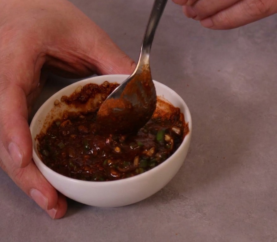 A thick, vibrant red spicy dipping sauce being stirred with a metal spoon in a small ceramic bowl.