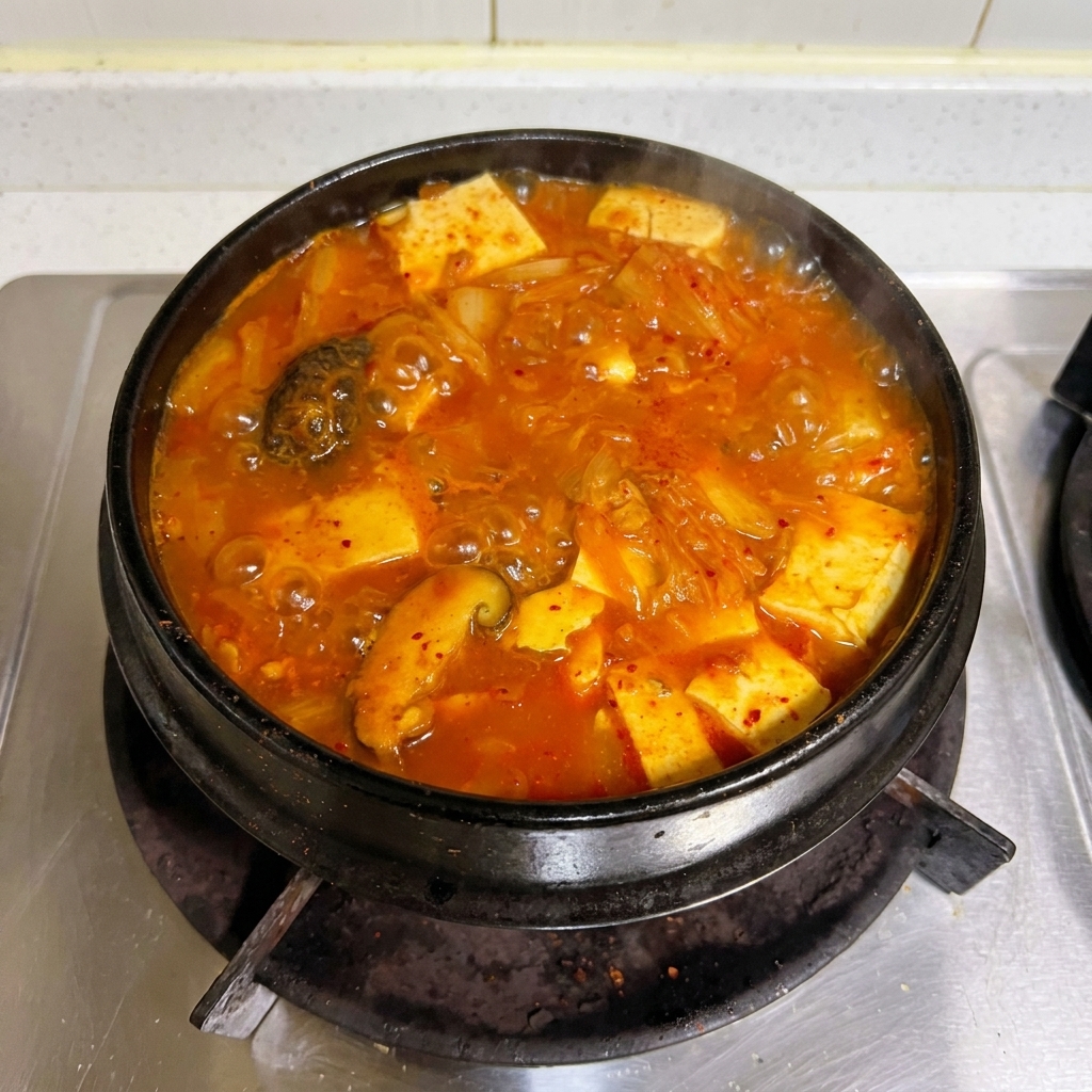 A vibrant red kimchi and tuna stew bubbling vigorously in a traditional stone pot on the stove.