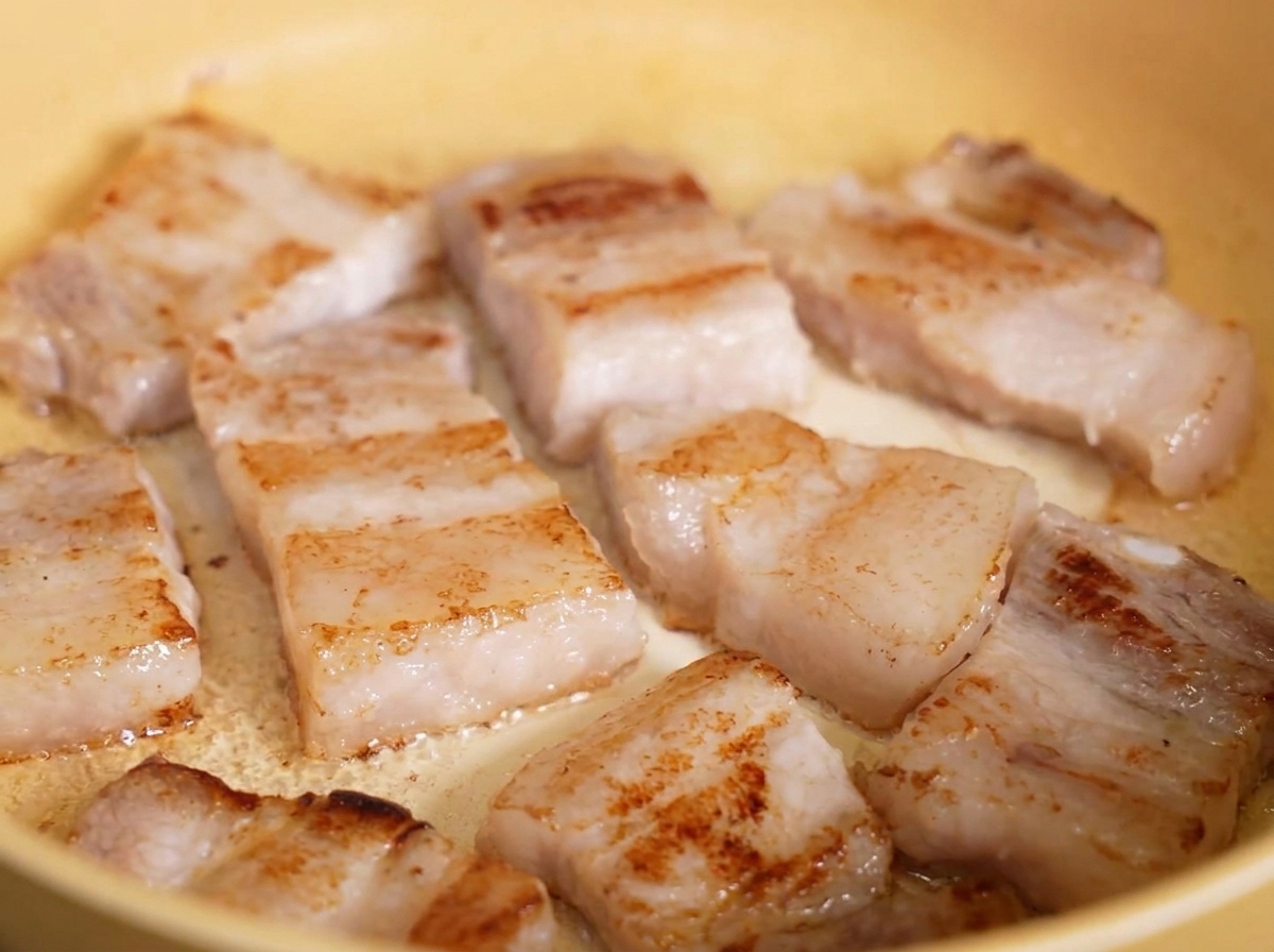 Crispy, golden-brown fried pork belly slices sizzling in rendered fat inside a yellow pan.