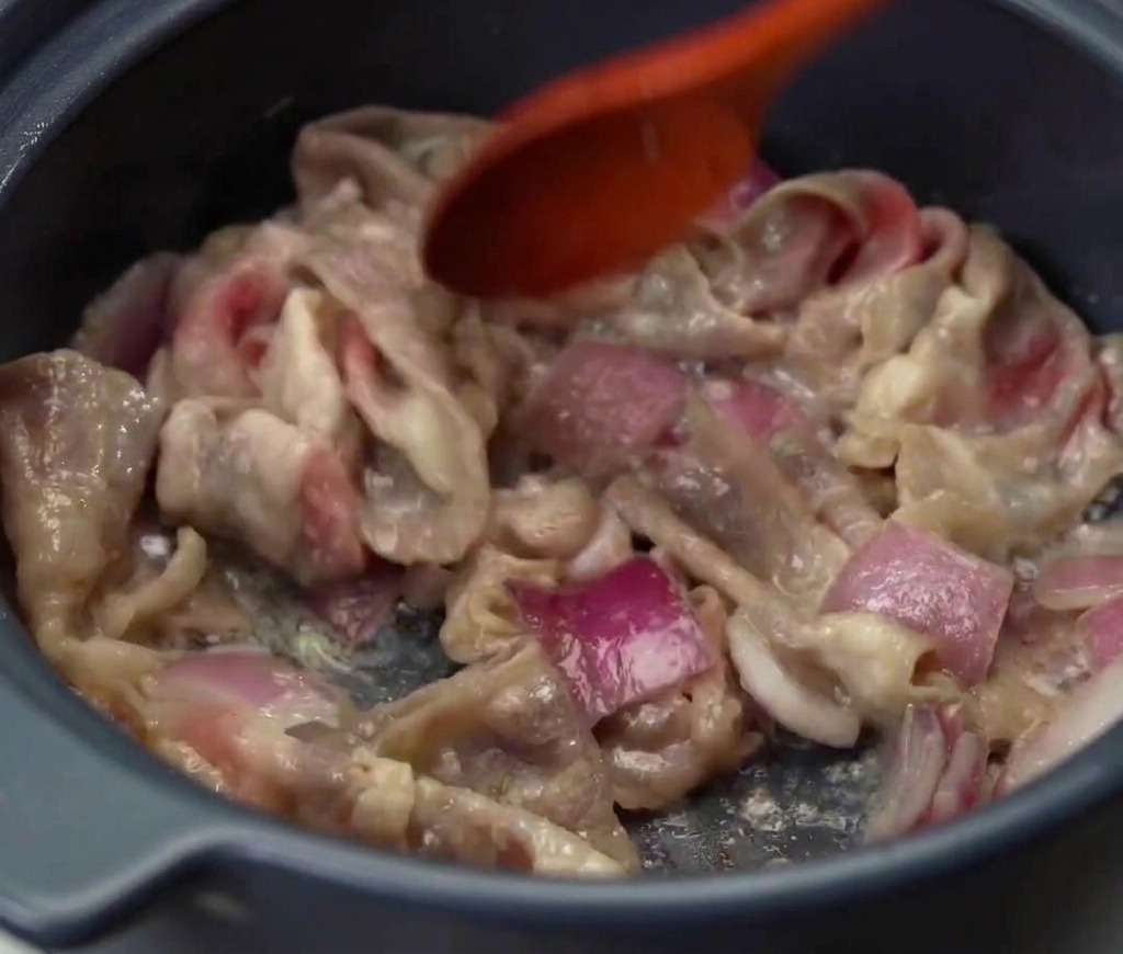 Sliced beef and purple onions being stir-fried together in a pot until the meat is cooked through and browned.