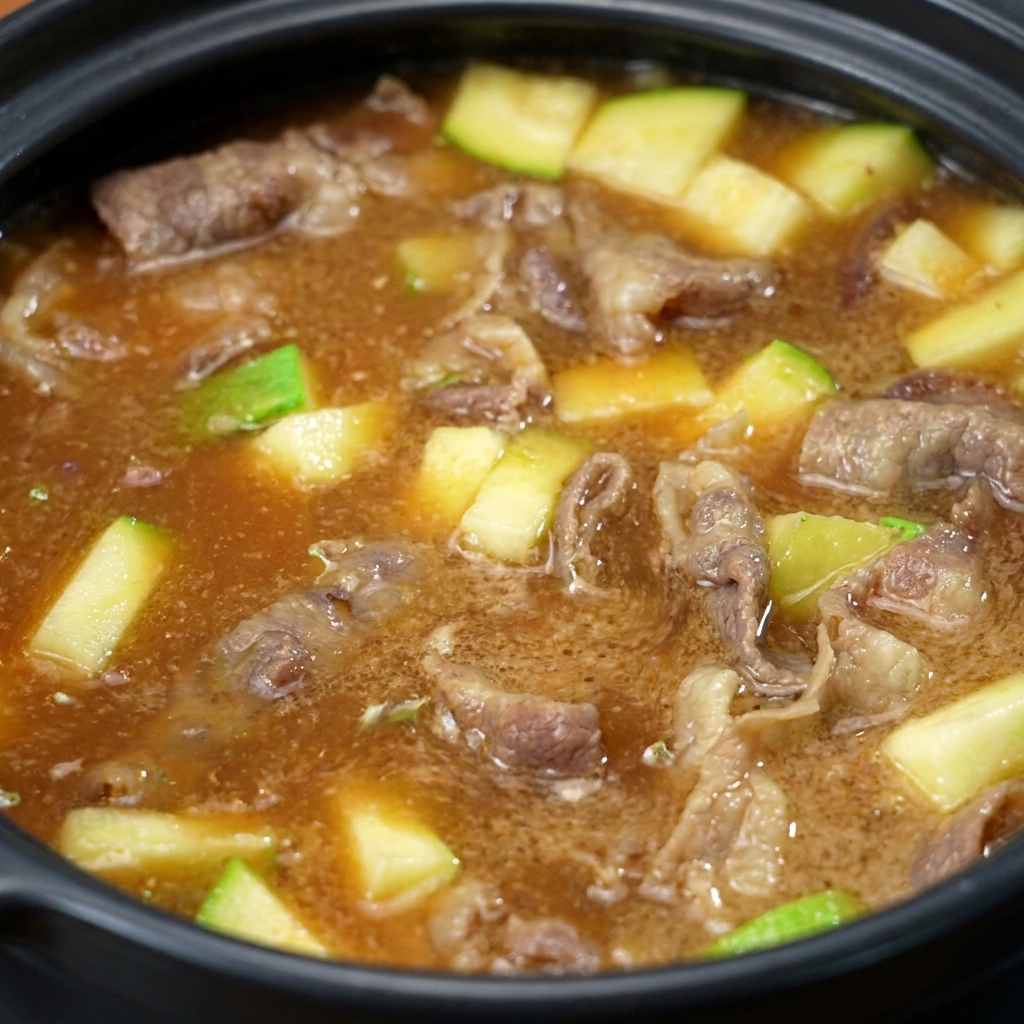 The soybean paste swirling and dissolving into the pot, turning the liquid into a cloudy brown broth with visible pieces of beef and zucchini.