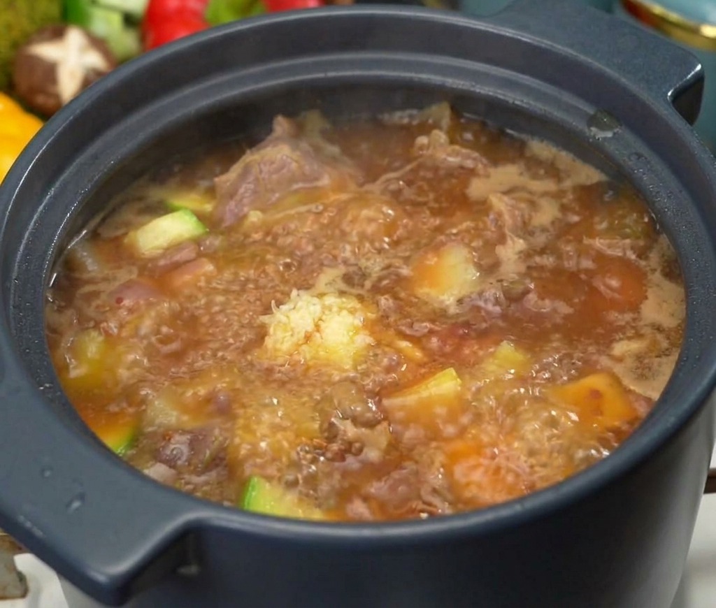 A spoonful of minced garlic sits atop a bubbling pot of Korean beef soybean paste soup with visible pieces of beef and zucchini.