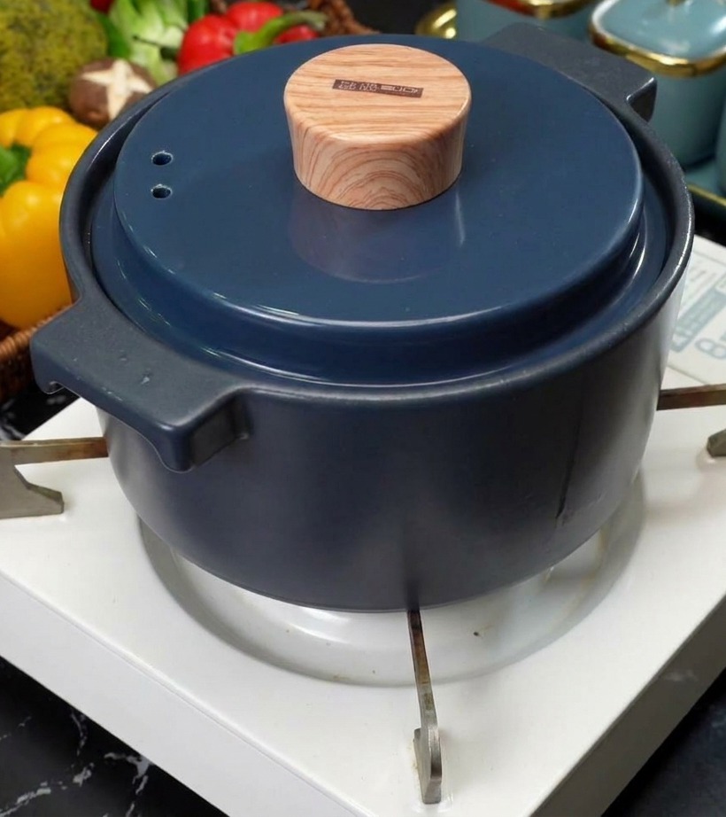 A blue ceramic pot with a stylish wood-look lid sitting on a white portable stove burner.