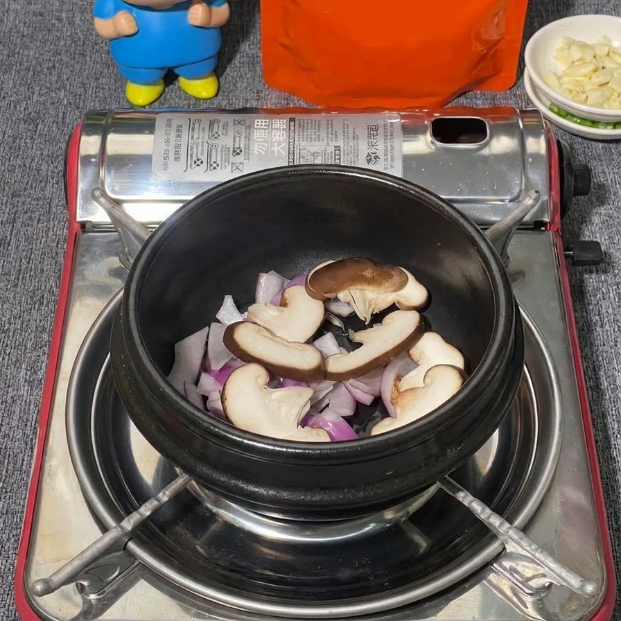 A variety of mushrooms including sliced shiitake and clusters of white shimeji mushrooms being layered in a black stone pot over red onions.