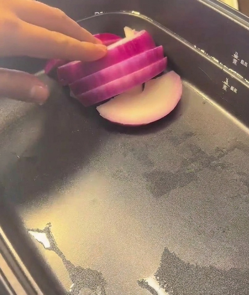 A hand placing vibrant slices of red onion into the base of a black electric cooking pot.