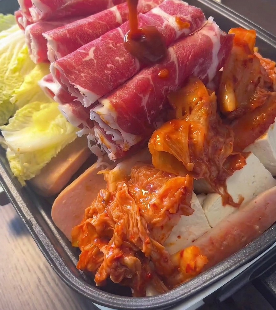 A pile of bright red, fermented kimchi placed in the center of a pot filled with meat and vegetables.