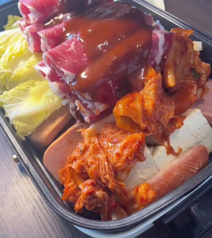 Rich, red Korean chili sauce being drizzled over a pot layered with beef, kimchi, and vegetables.