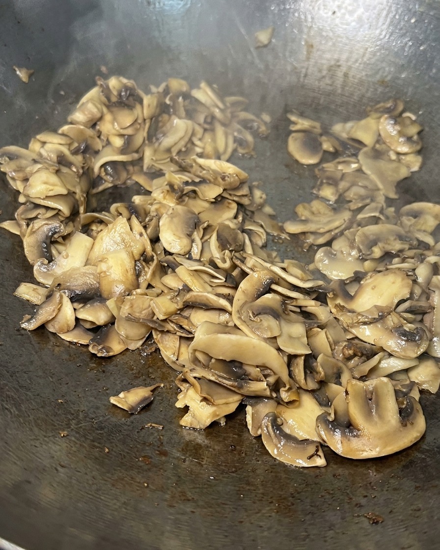 Sautéed mushroom slices in a pan, now cooked down until they are golden brown and mostly dry.